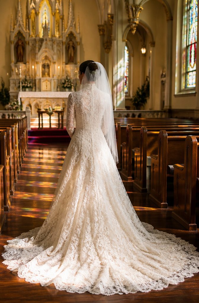 A lace gown with long sleeves and high neckline in a church setting.