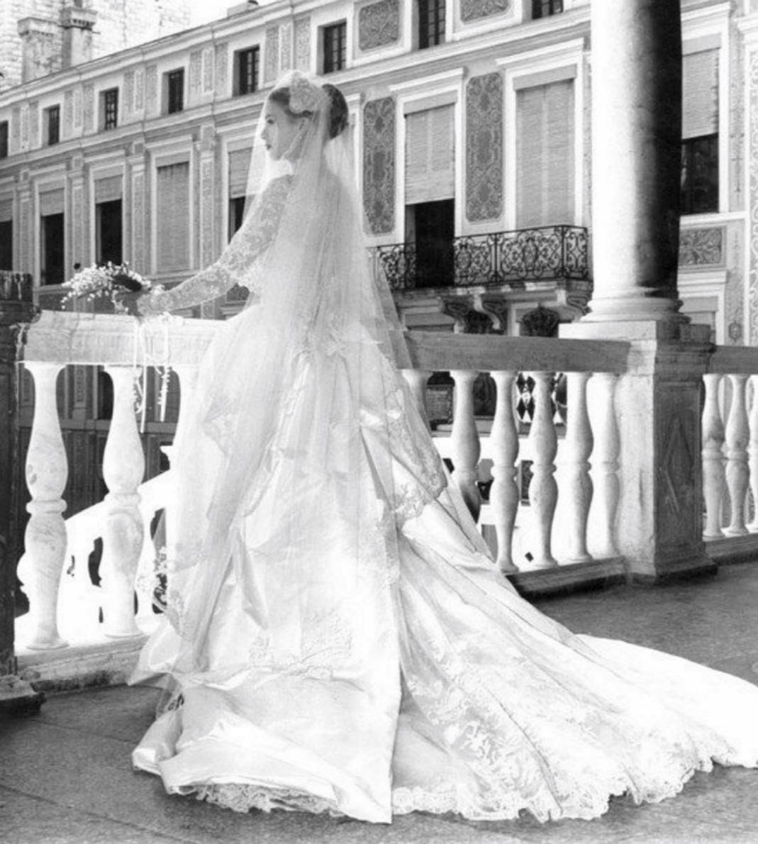 Woman in a white wedding gown with lace sleeves and long veil on balcony.