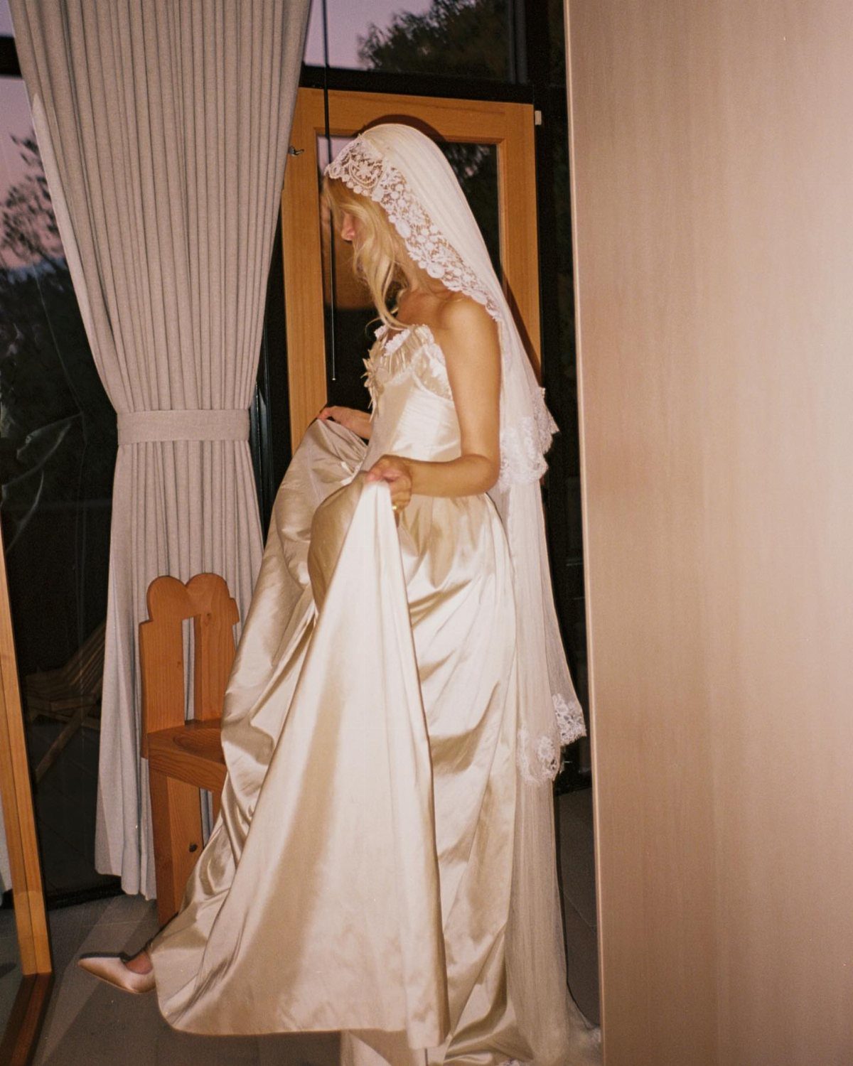 Woman in a white satin wedding gown wearing a matching lace-edged veil.