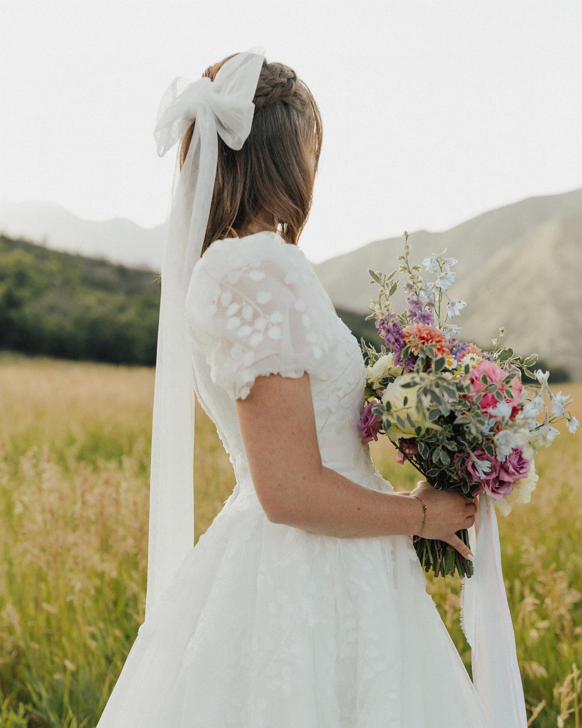 Woman in white wedding dress with puffed sleeves holding a colorful flower bouquet.