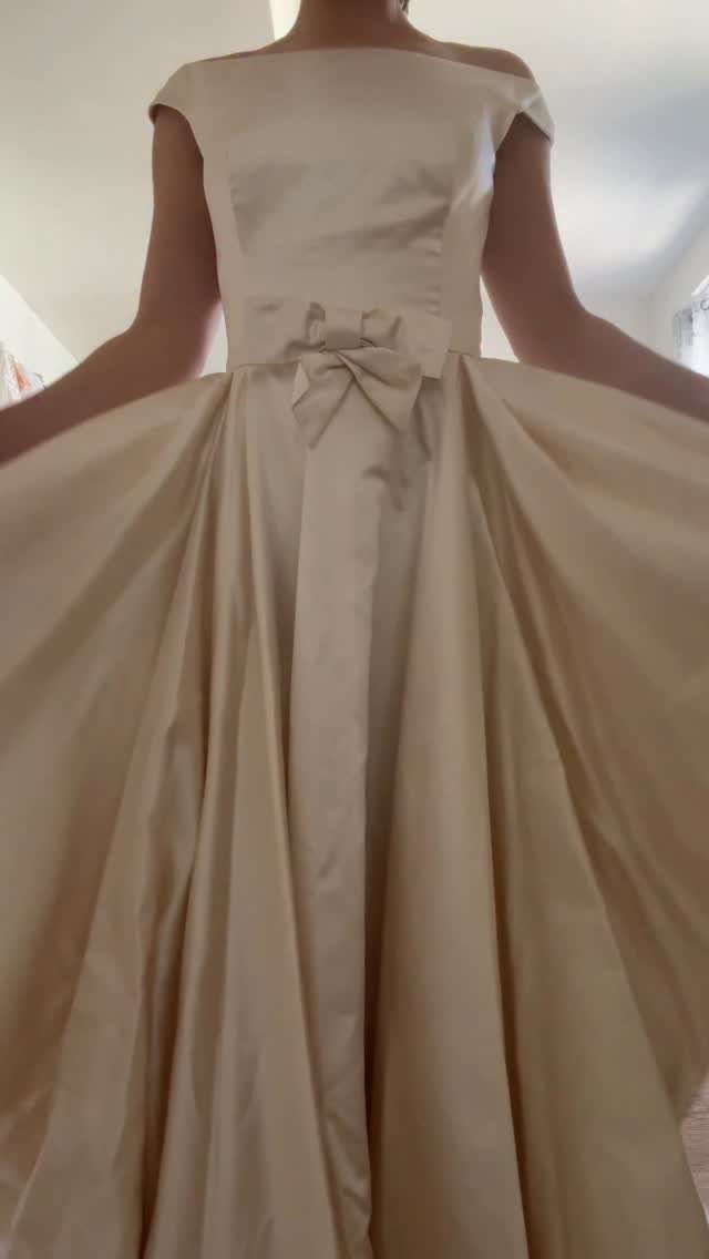 Cream satin wedding dress with off-the-shoulder neckline and a large bow at waist.