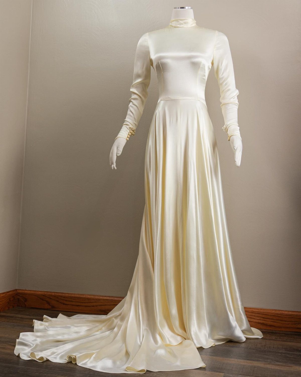 Cream satin wedding gown with long sleeves and high neck on a mannequin