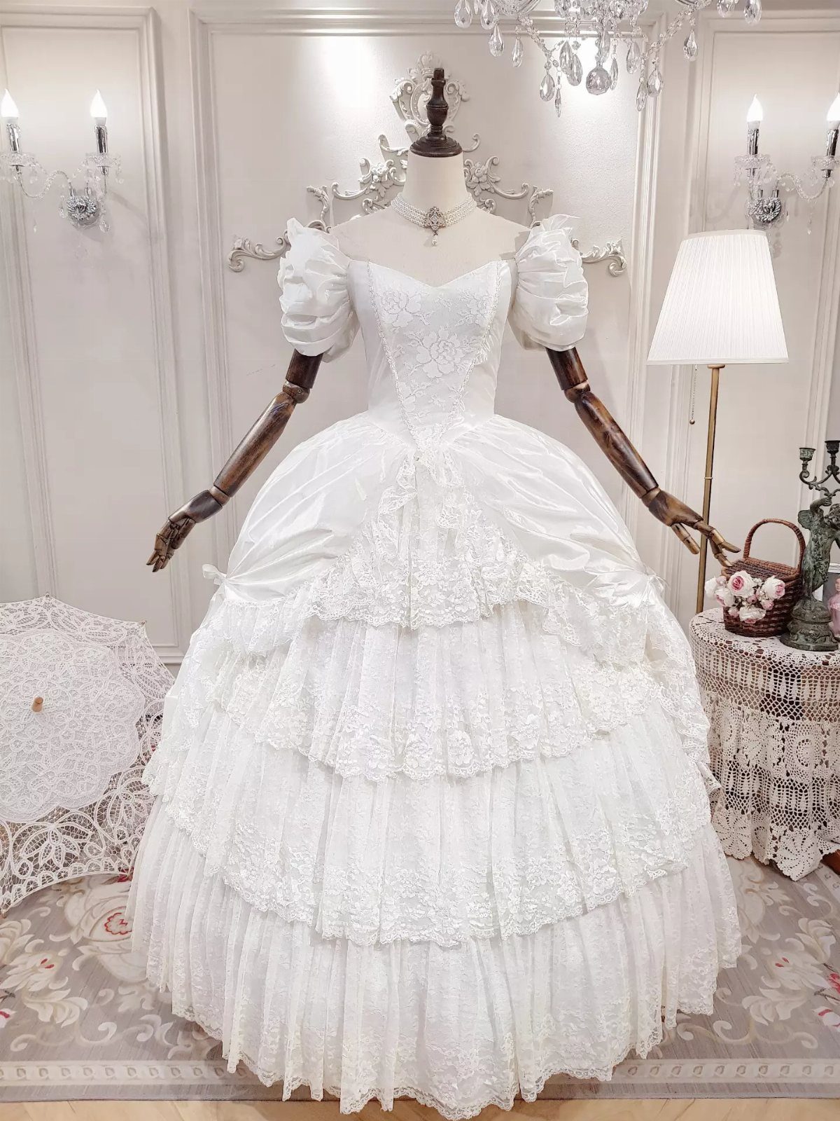 White wedding dress on a mannequin with a tiered lace skirt and puffed sleeves.