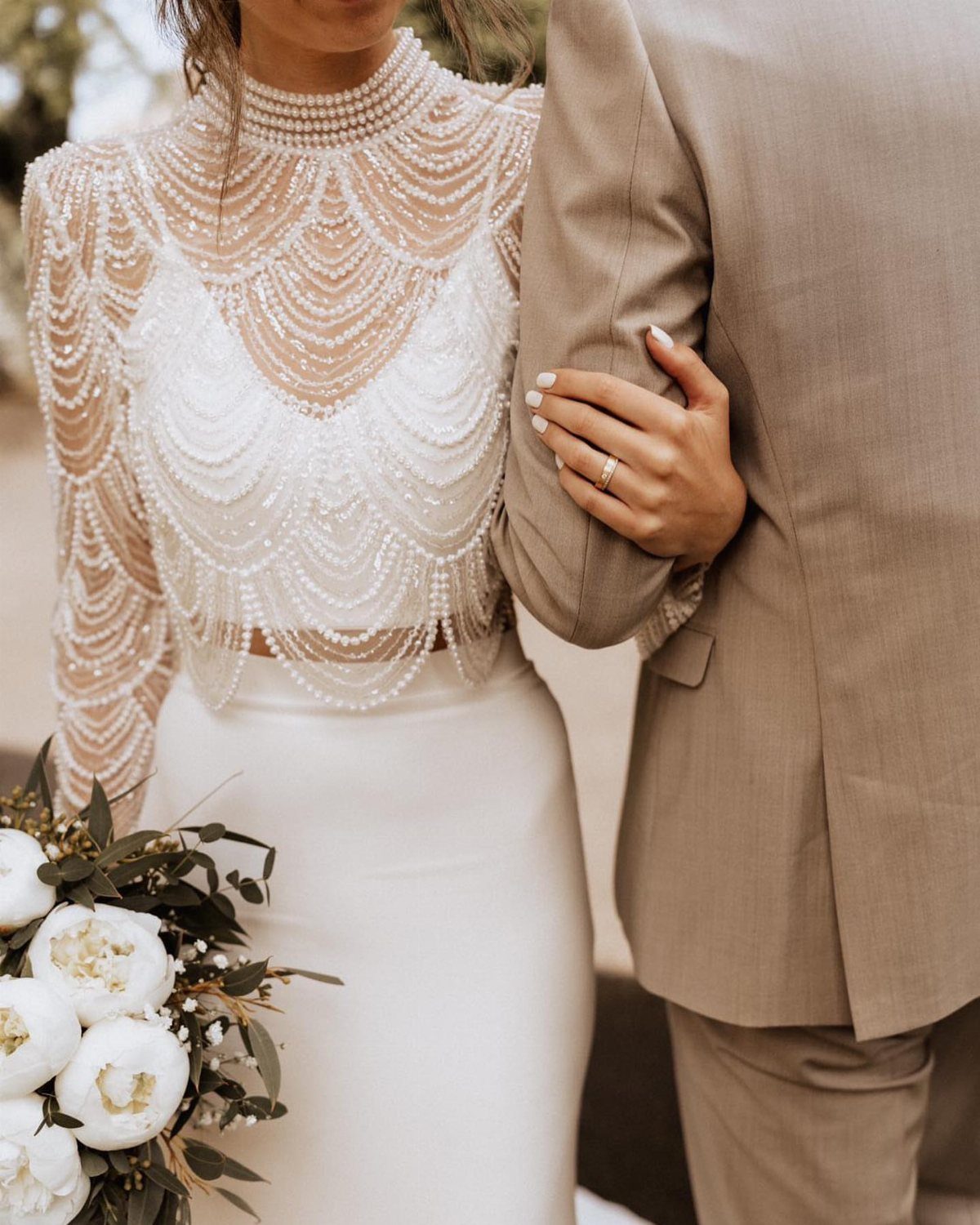 Bride in beaded bridal separates and groom in tan suit holding white flowers