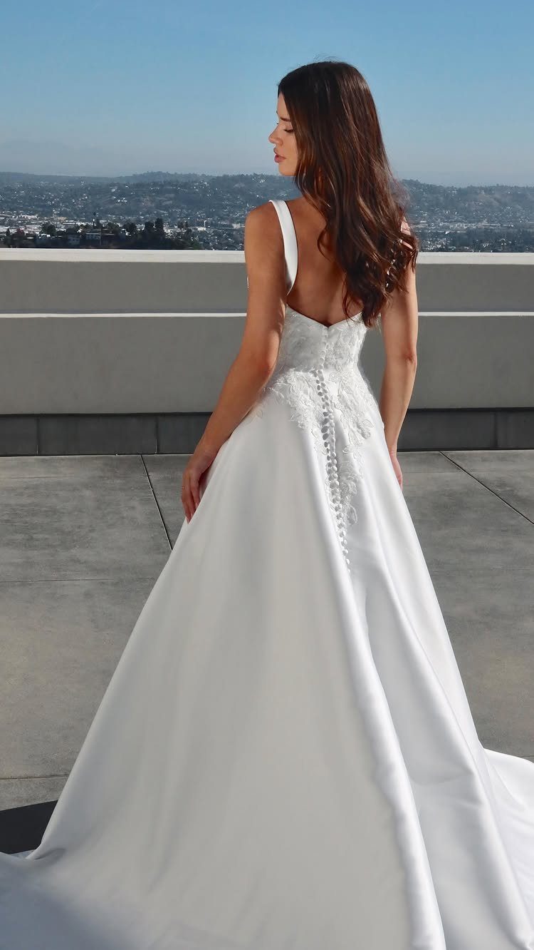 Woman in a white satin A-line wedding gown standing on a rooftop terrace.