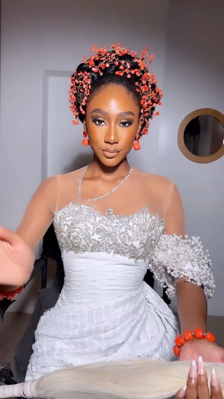 Woman in white bridal gown wearing red beaded headpiece, earrings, and bracelet.