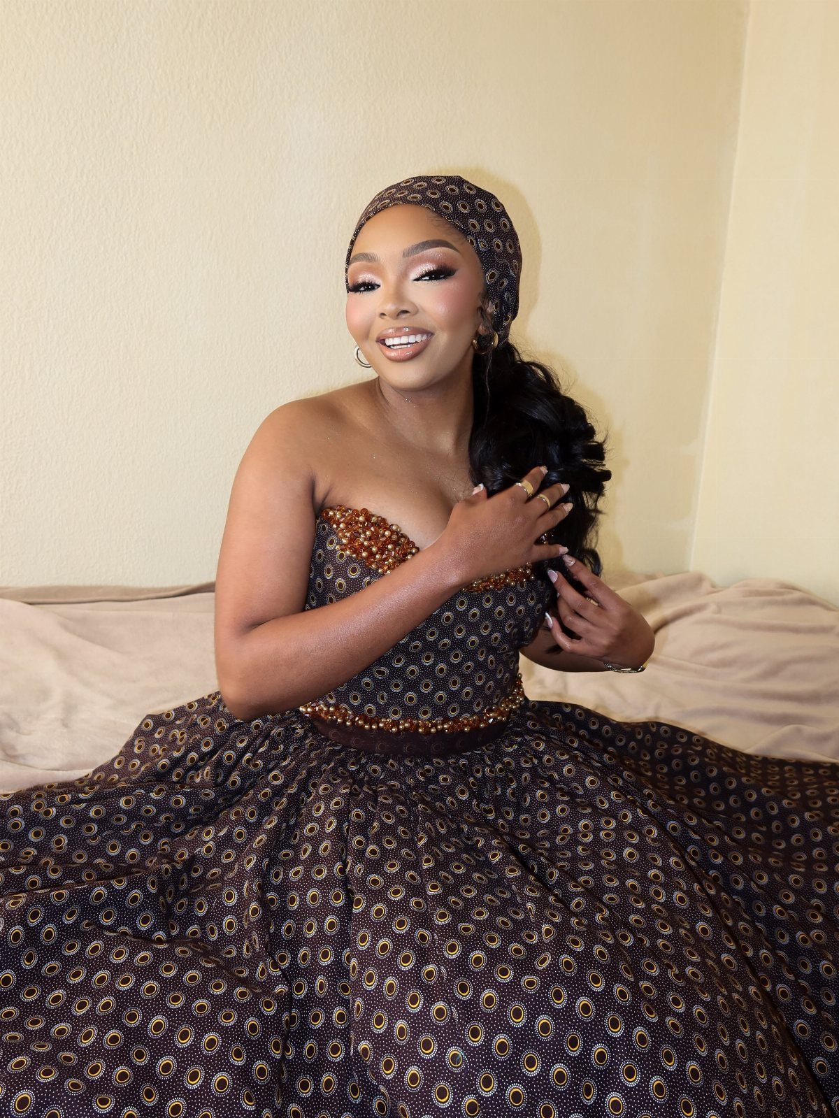 Woman in a strapless brown and gold patterned bridal gown and matching headwrap.