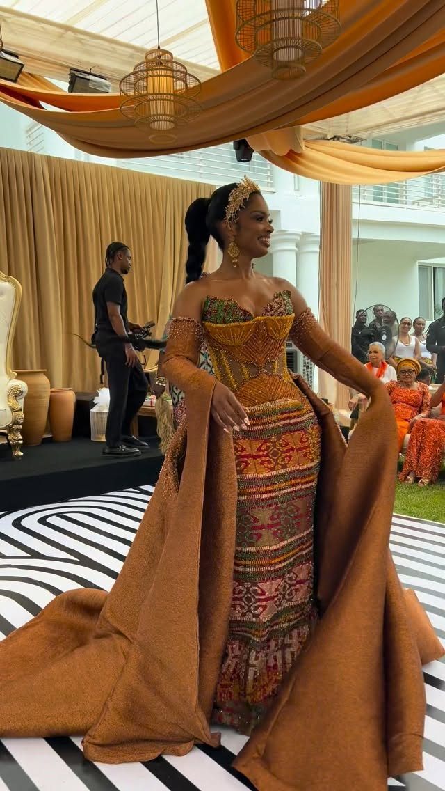 Woman in a gold Kente cloth bridal gown with a long flowing cape