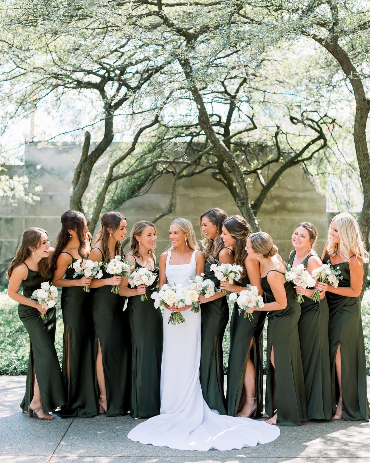 Bride in white gown surrounded by bridesmaids in emerald green floor-length dresses.