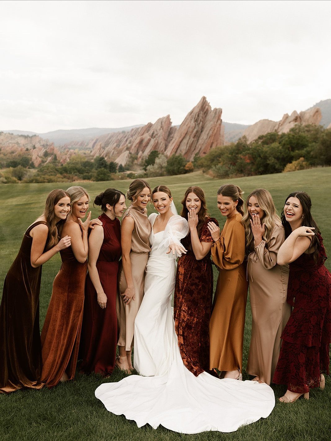 Bride and bridesmaids in floor-length autumn colored dresses posing before red rock mountains.