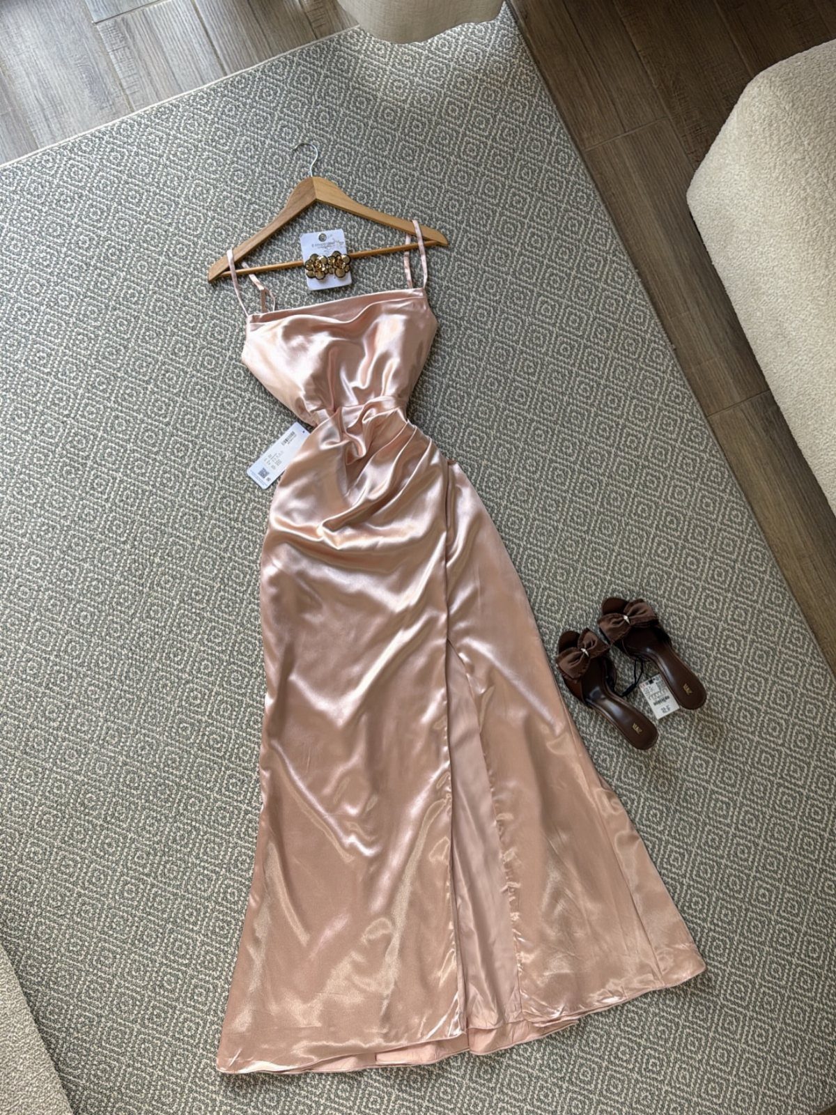 Champagne satin bridesmaid dress on a hanger with brown heels on a rug