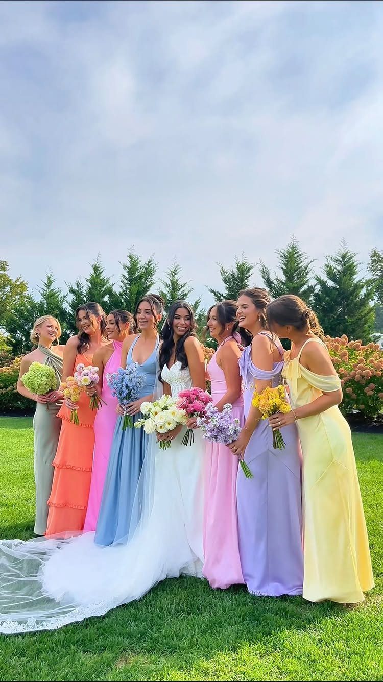 Bride and bridesmaids in colorful pastel dresses posing on a green lawn.