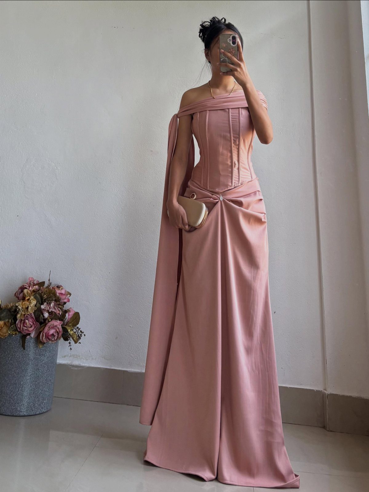 Woman in a dusty rose satin one-shoulder gown posing for a mirror selfie.