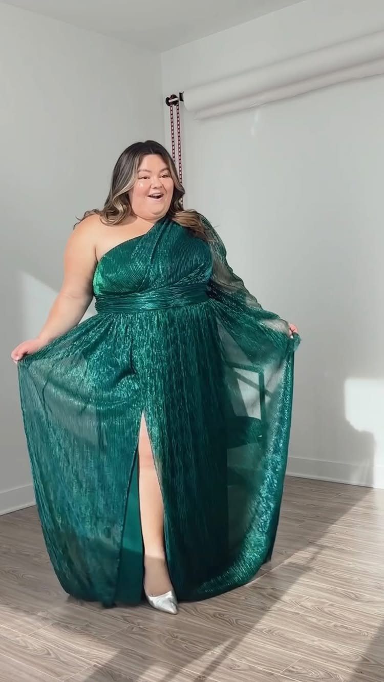 Plus-size woman wearing a shimmering emerald green one-shoulder floor-length bridesmaid gown.