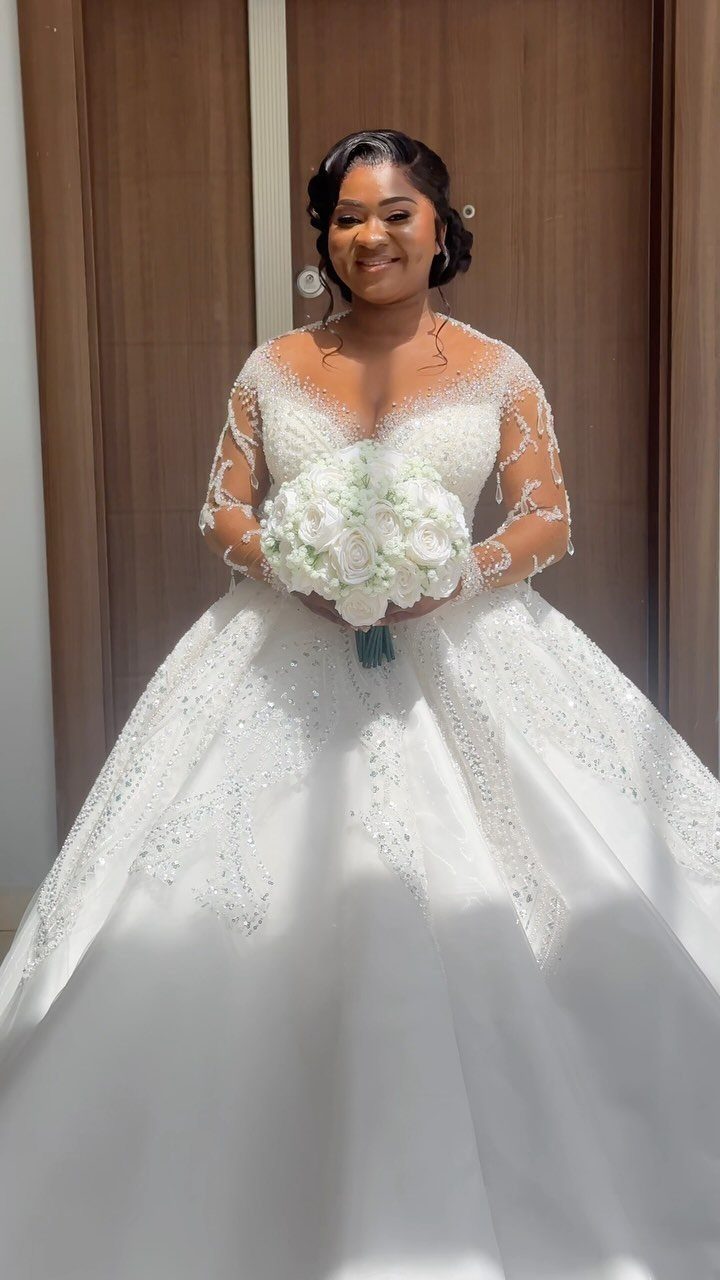 Woman in a beaded white ballroom wedding gown holding a white floral bouquet.