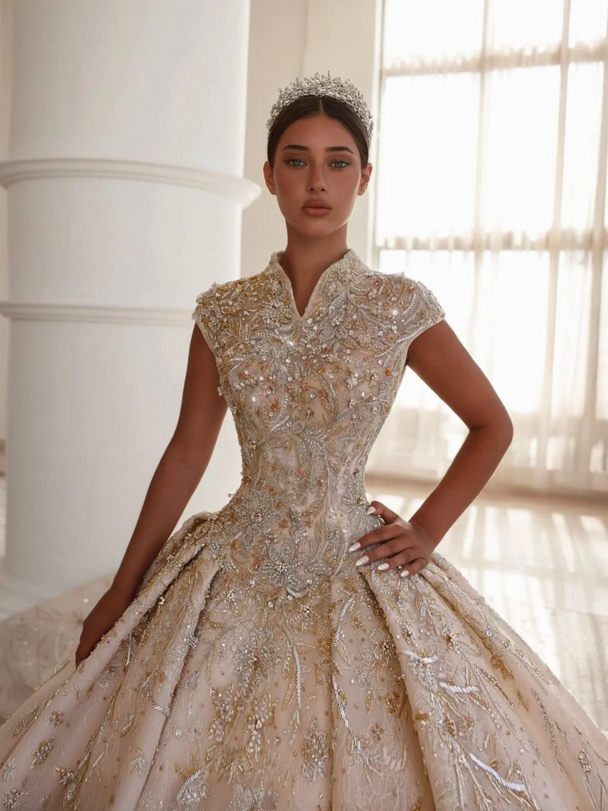 Woman in a champagne embellished ballroom wedding gown and tiara posing indoors.