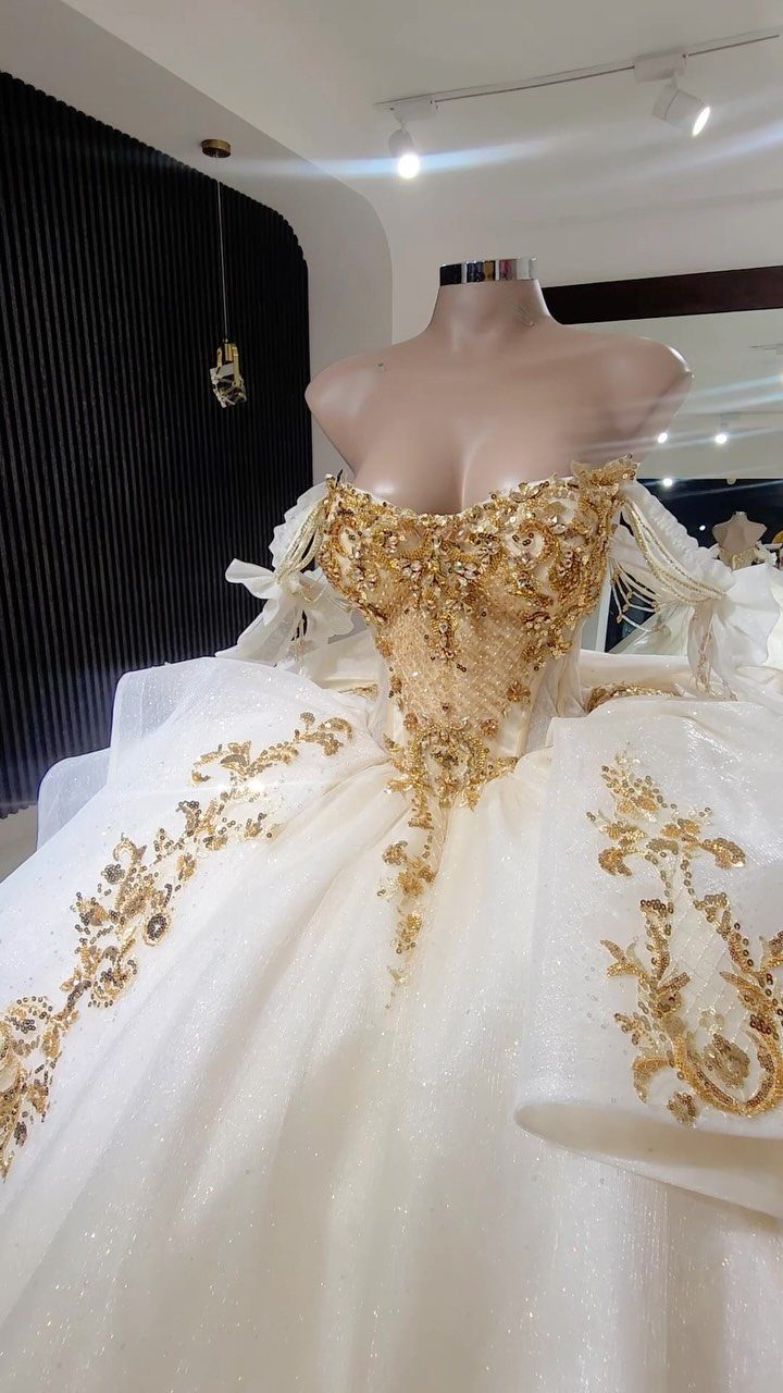 White ballroom wedding gown with gold embroidery displayed on a studio mannequin.