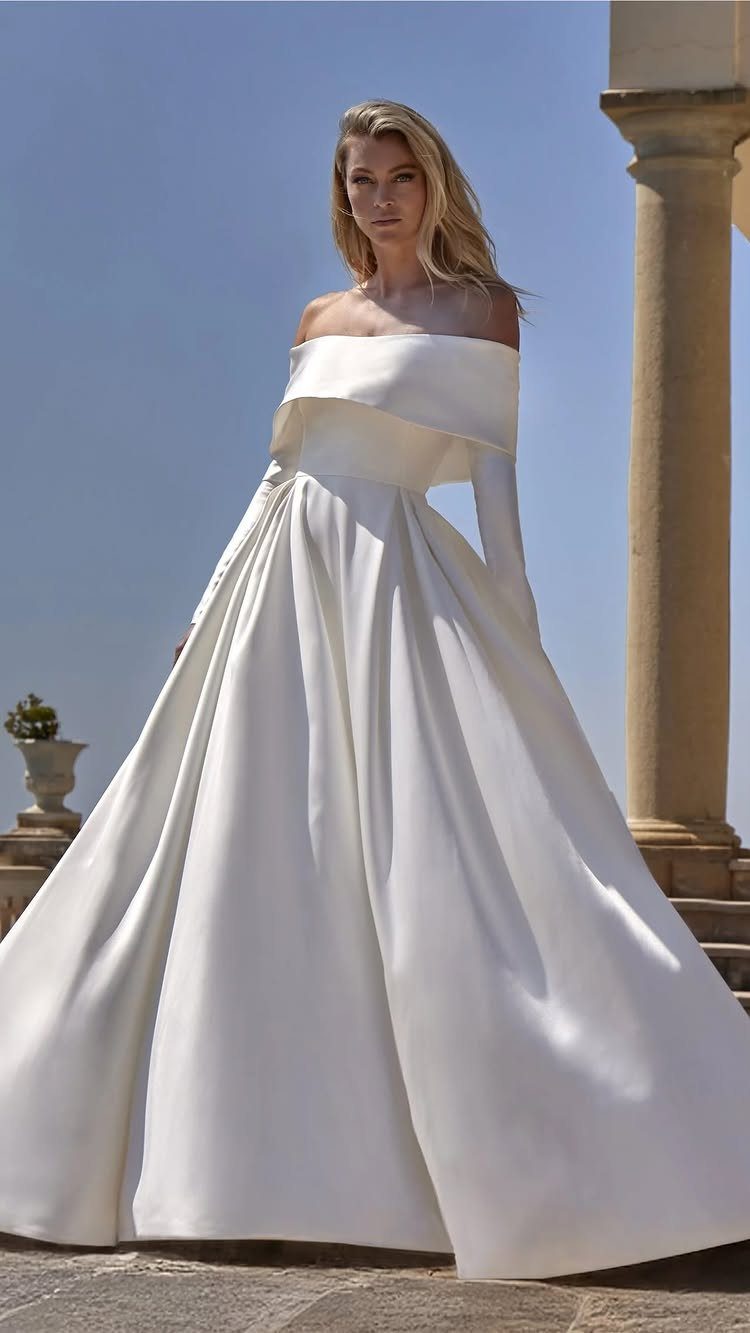 Woman in a structured white satin ball gown standing on a stone terrace.