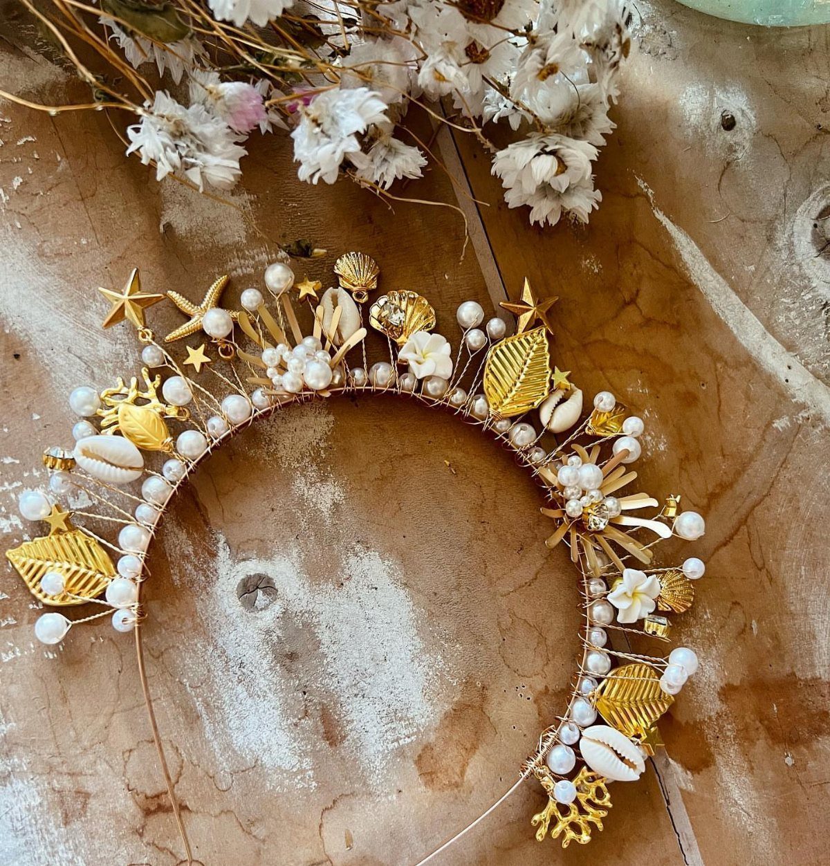 Gold headband with pearls and seashells resting on a brown textured surface.