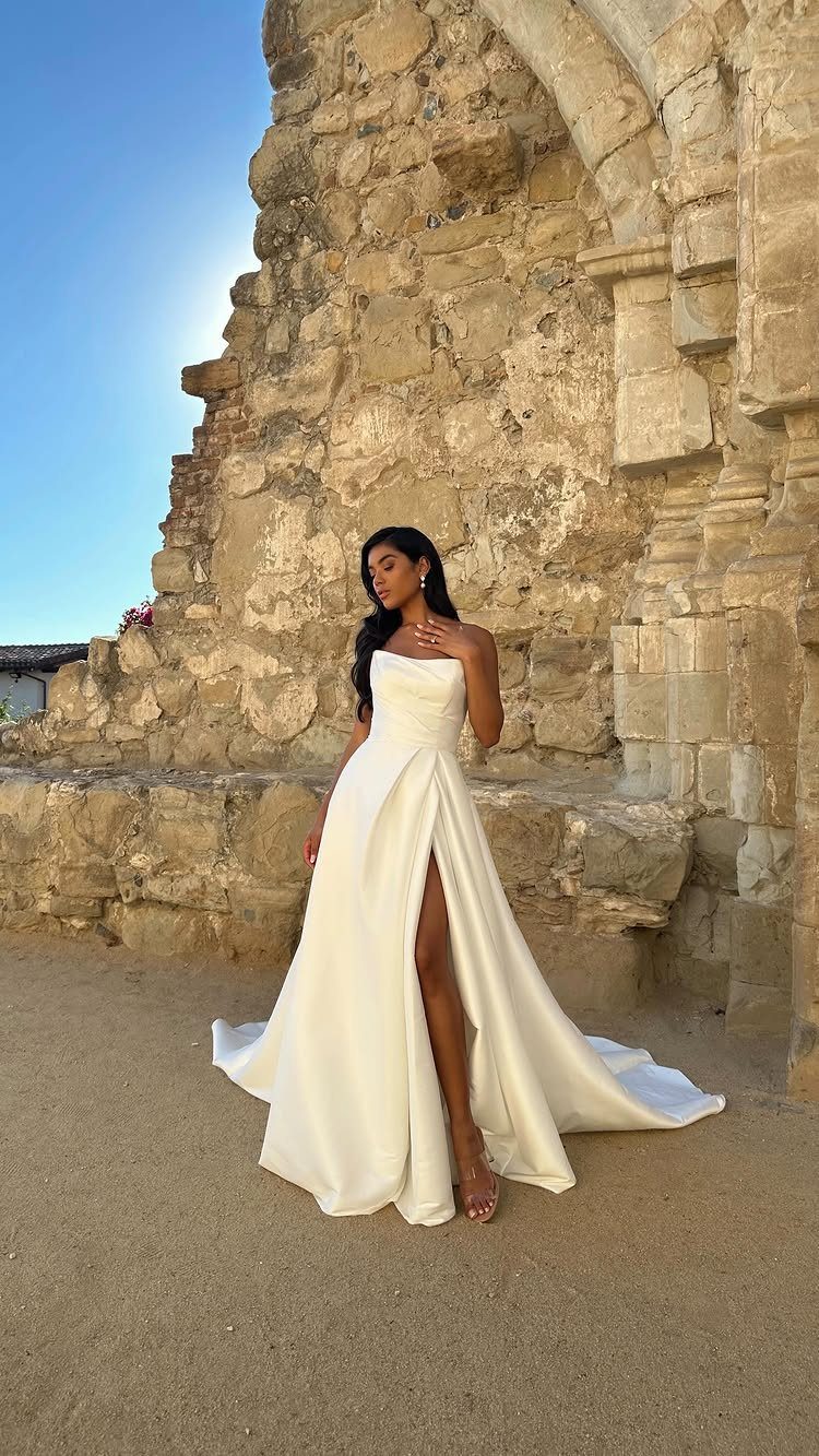 Woman in a sleek strapless white wedding gown posing by stone ruins.