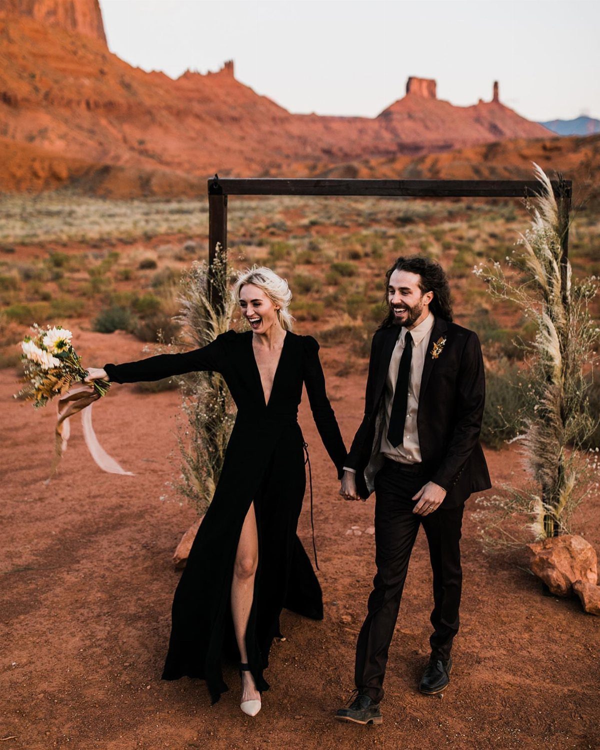 Couple walking in a desert, woman wearing a long-sleeved black wedding dress.
