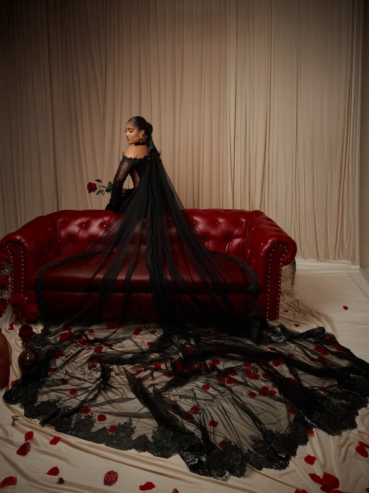 Woman in a black lace wedding gown and veil standing by red sofa