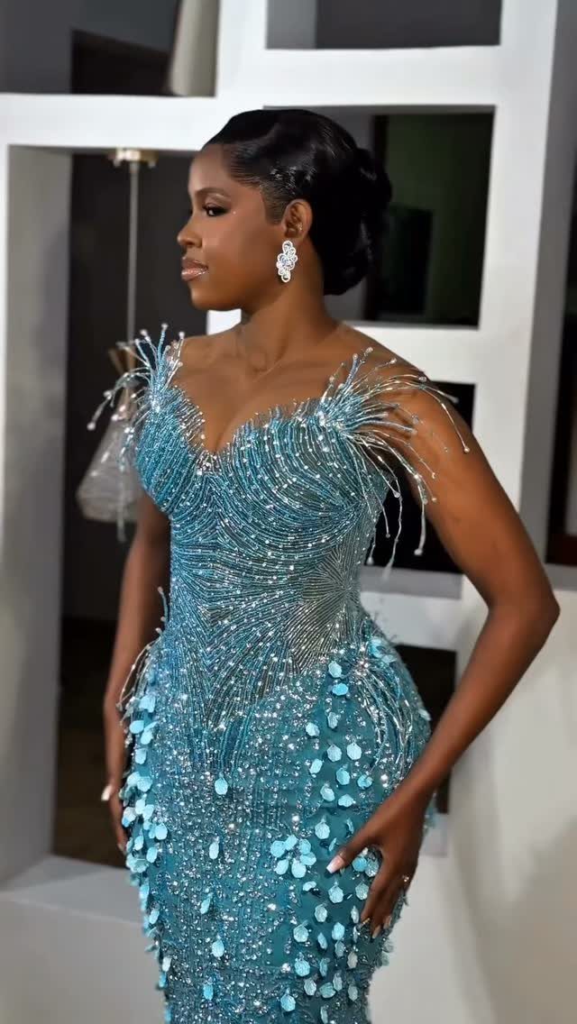 Woman wearing a shimmering teal-blue bridal gown with 3D floral details and beaded shoulders.