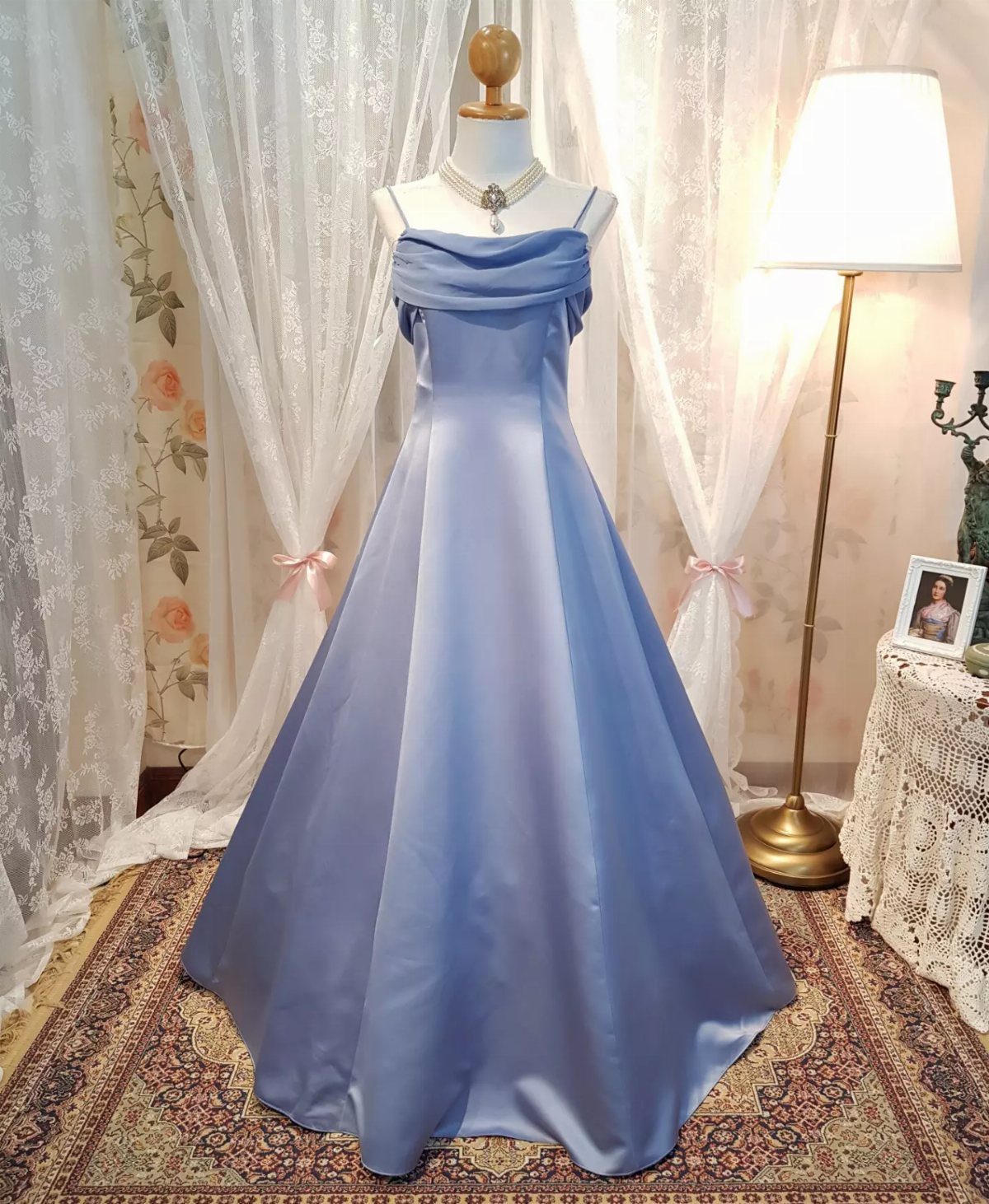 Light blue satin wedding dress on a mannequin in a lace-curtained room