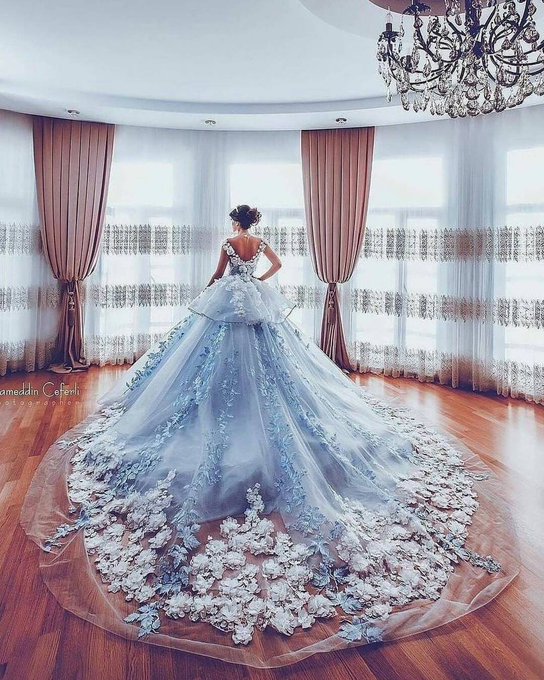 Woman in a voluminous light blue ball gown with floral lace train and embellishments.