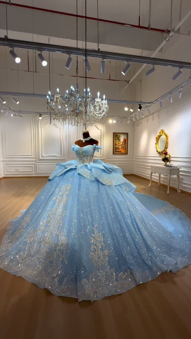 Light blue ballgown with gold glitter embroidery displayed on a mannequin under a chandelier.