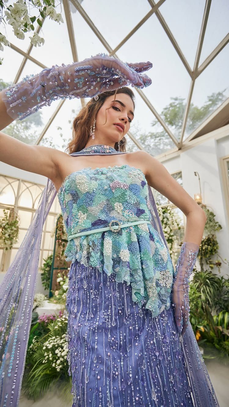 Woman in a two-tone blue and purple sequined gown posing in a glass conservatory.