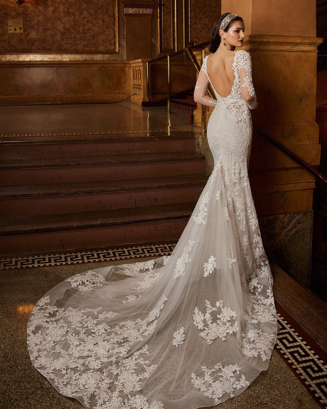 Woman in a white lace wedding dress with a deep open back and long train.