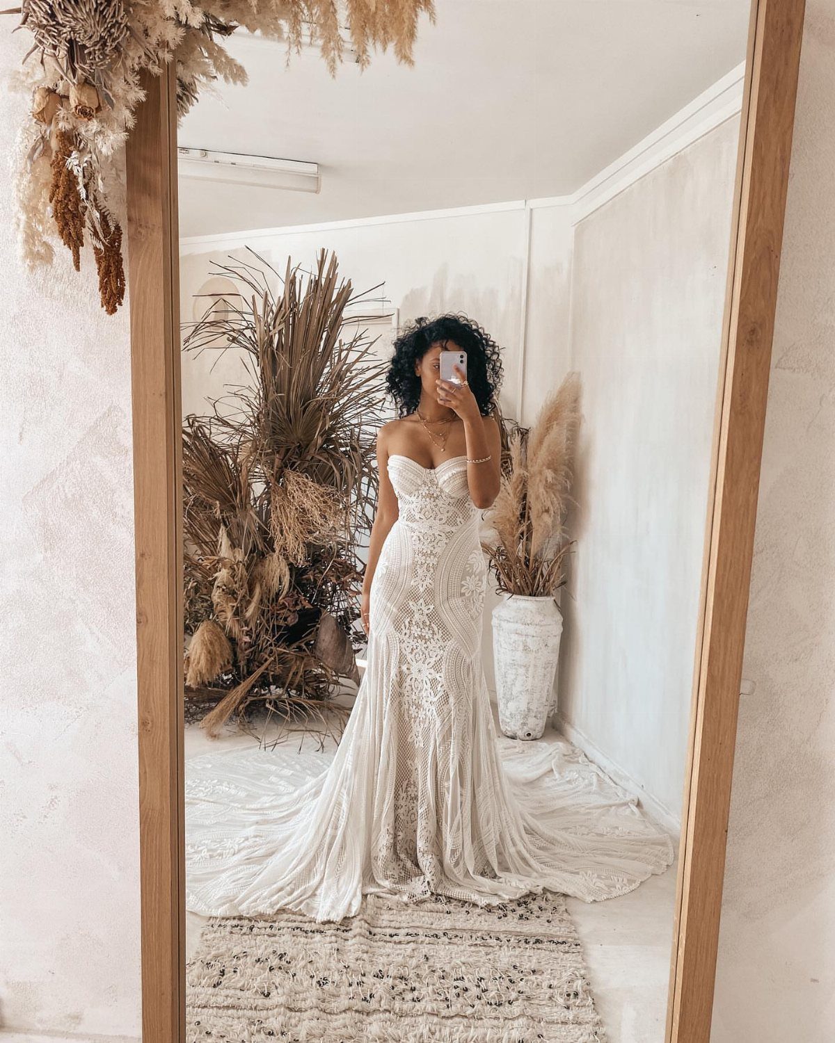 Woman in a white lace strapless boho bridal gown posing for a mirror selfie.