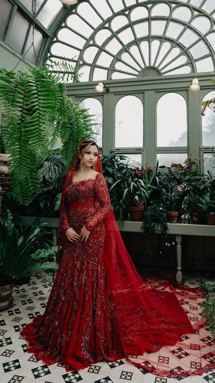 Woman in a red embellished mermaid bridal gown standing in a lush greenhouse