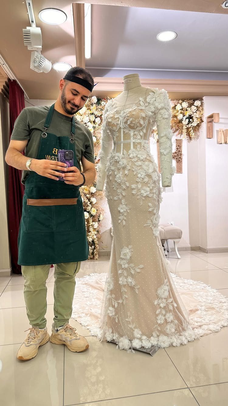 White lace mermaid bridal gown on a mannequin next to a male tailor.