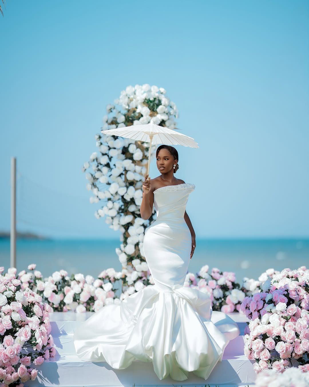 Woman in a white mermaid bridal gown holding a parasol by the ocean