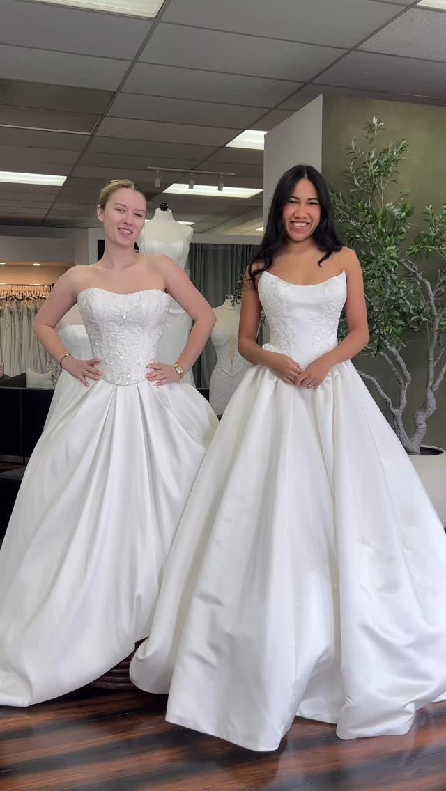 Two women wearing white strapless sweetheart neckline ball gown wedding dresses in a shop.