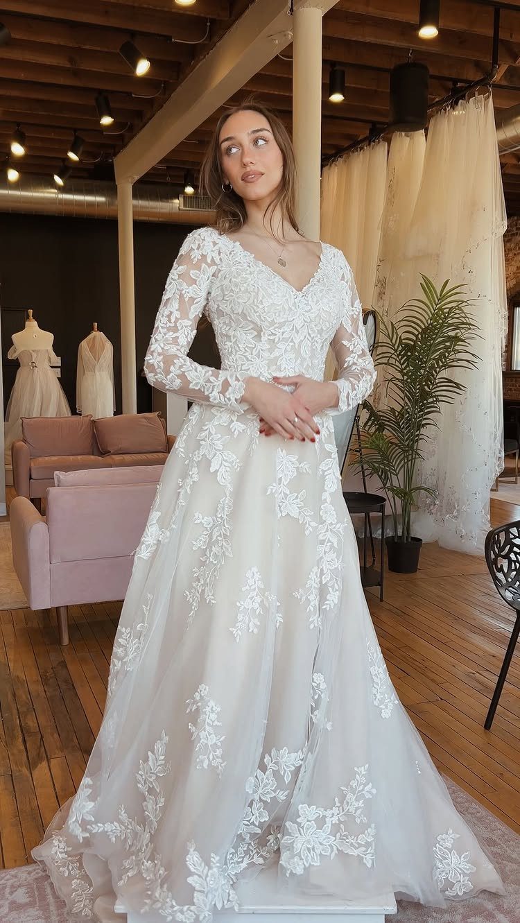 Woman in a white long-sleeved lace wedding dress standing in a bridal boutique.