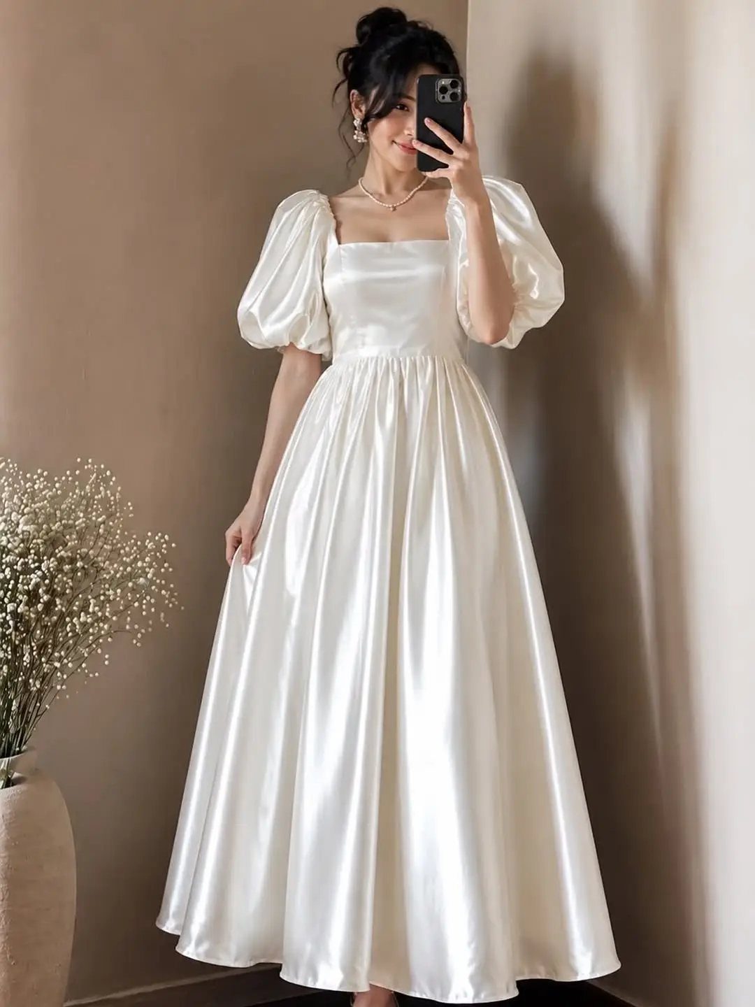 Woman in a white satin A-line dress with short puff sleeves taking a selfie.