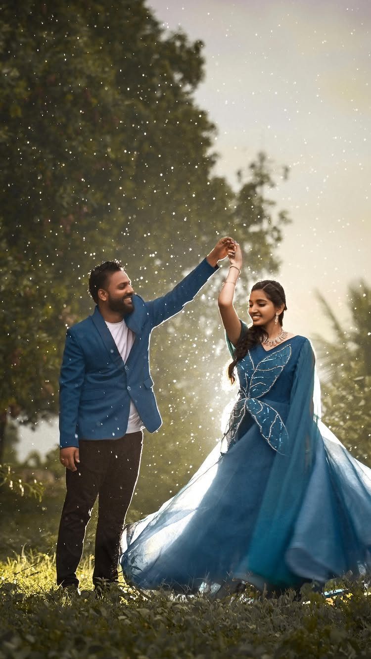Couple in blue attire dancing in a grassy field with lush green trees.