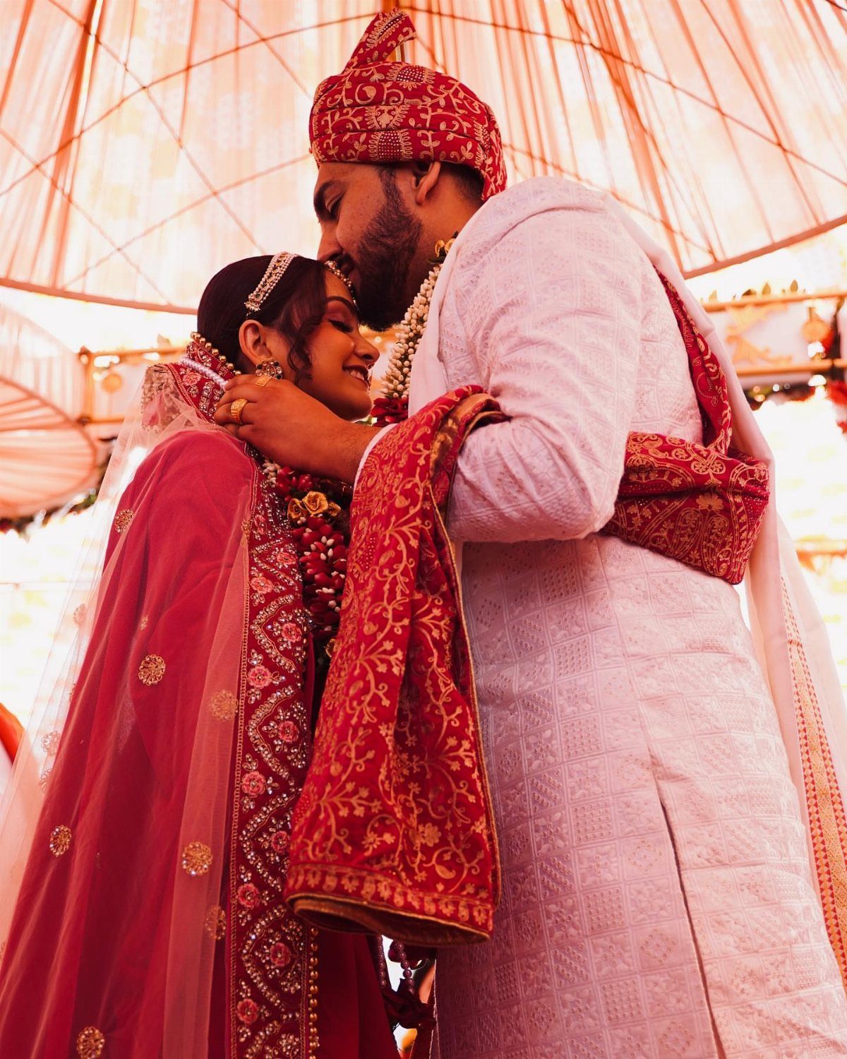 Bride and groom in traditional Indian wedding attire resting their foreheads together.