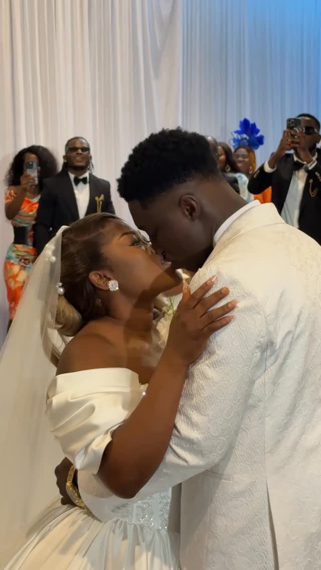Bride and groom kissing in white wedding attire with guests in the background
