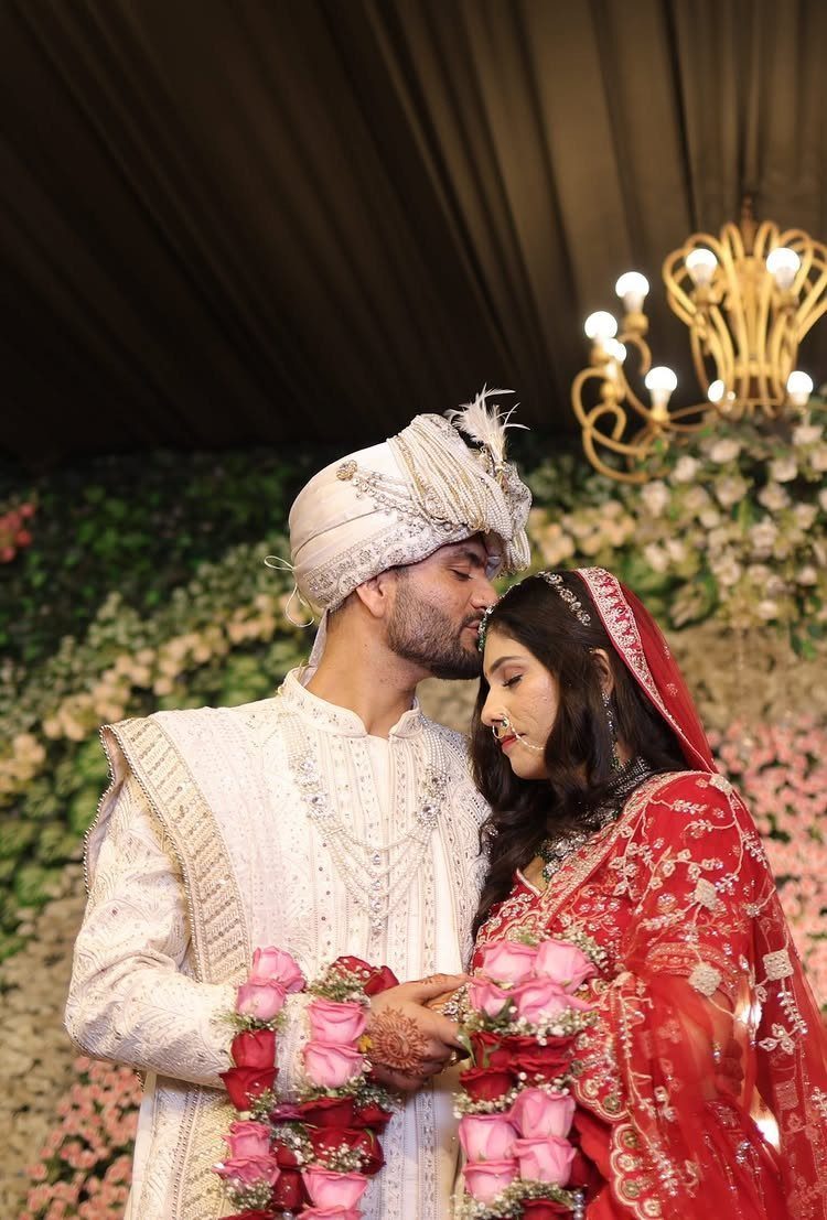 Groom in white sherwani kissing the forehead of a bride in red sari