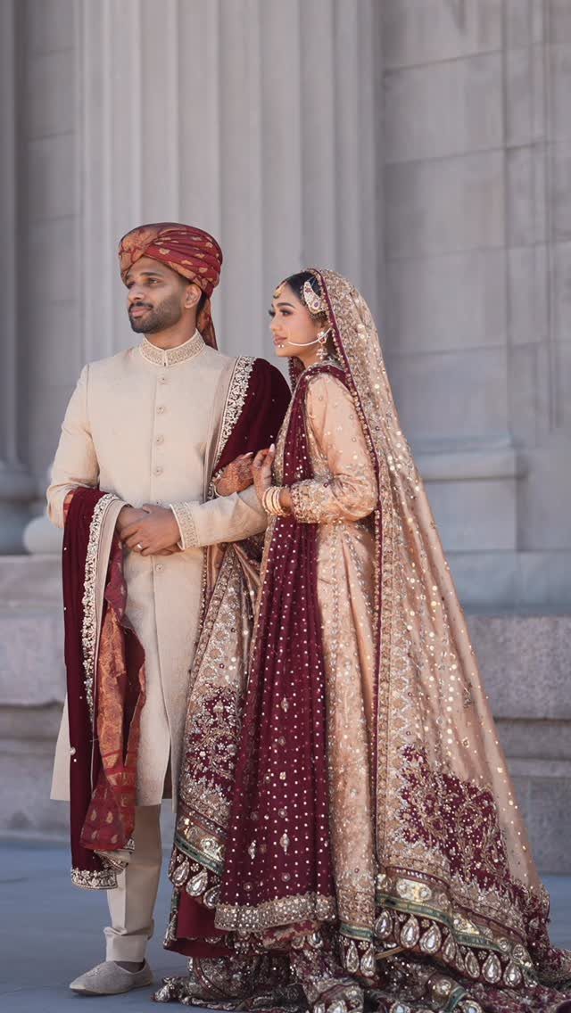 Bride and groom in traditional South Asian wedding attire standing before white columns.