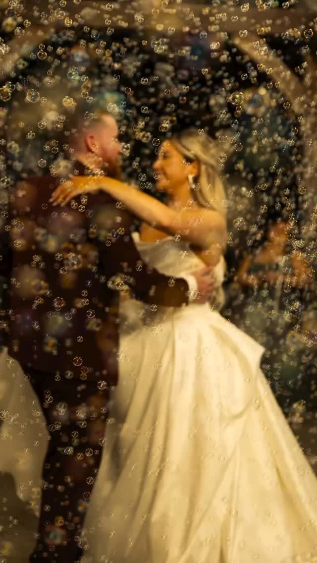 Bride and groom embracing and smiling while surrounded by floating bubbles at night.