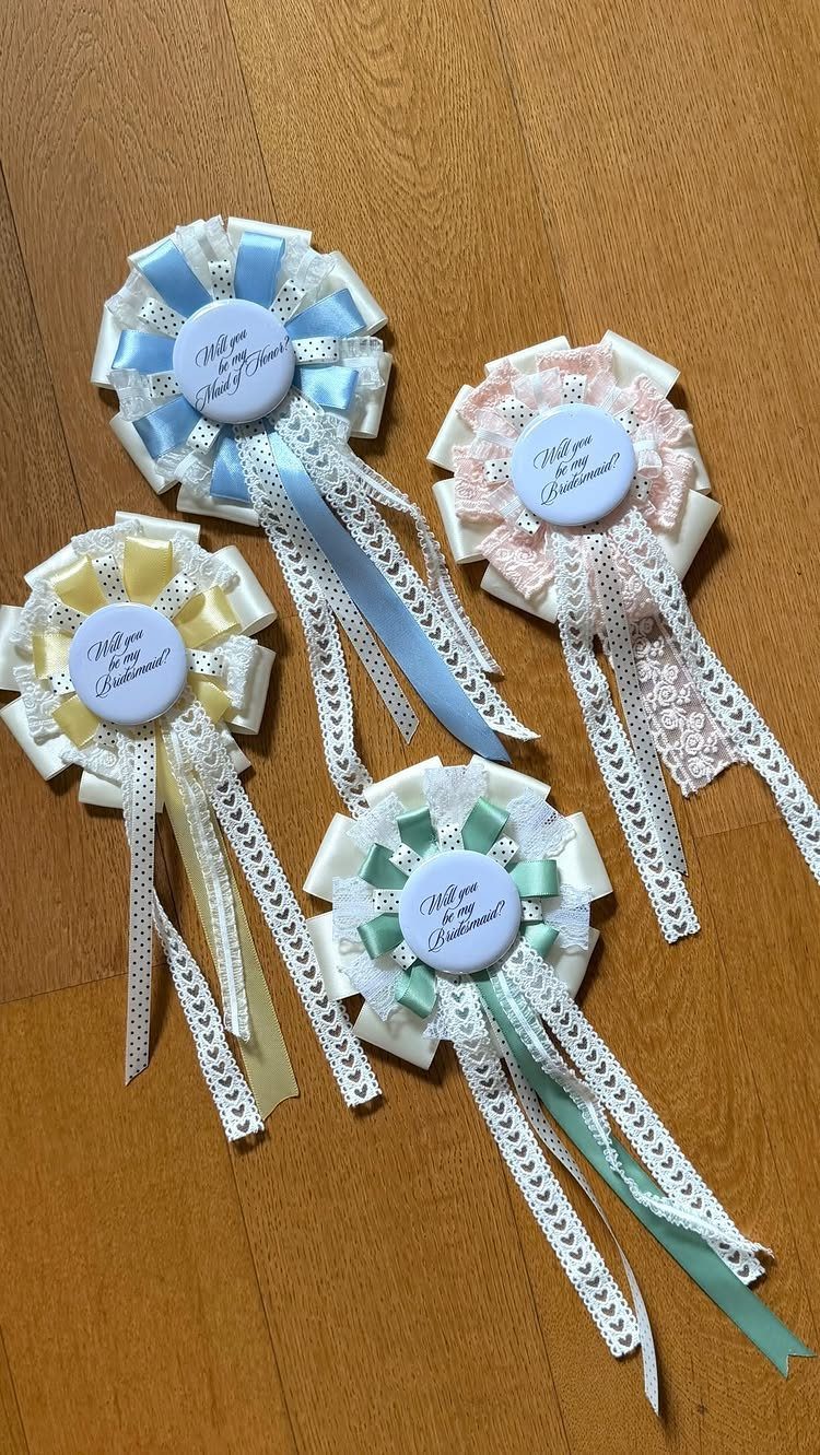 Four colorful fabric rosettes with ribbons and proposal buttons on a wooden floor.