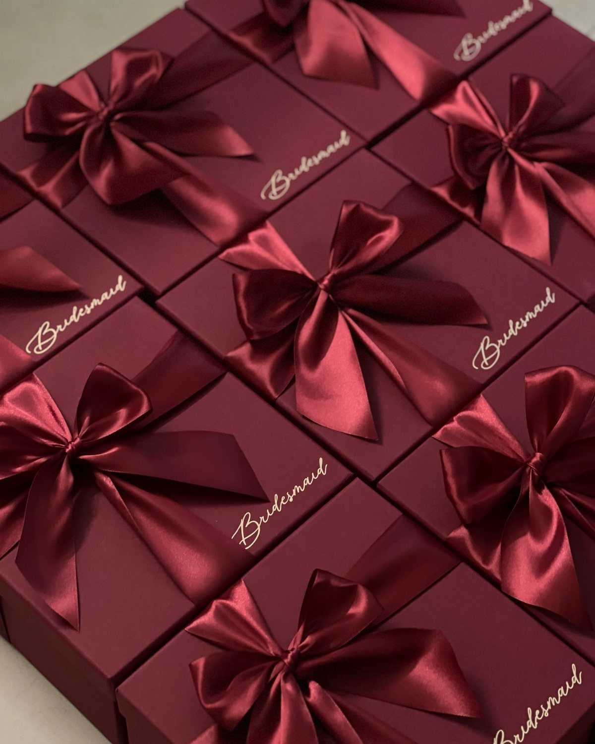 Burgundy bridesmaid proposal boxes with satin bows and gold cursive lettering.