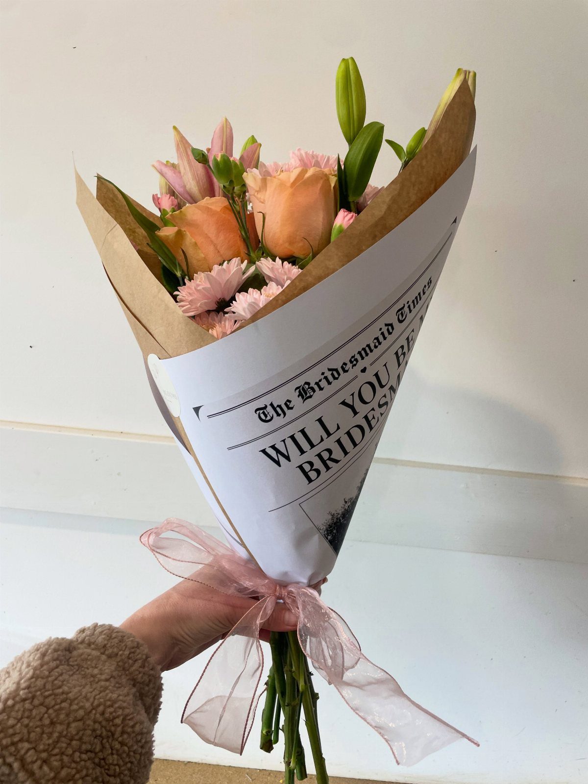 Bouquet of peach and pink flowers wrapped in a bridesmaid proposal sleeve.