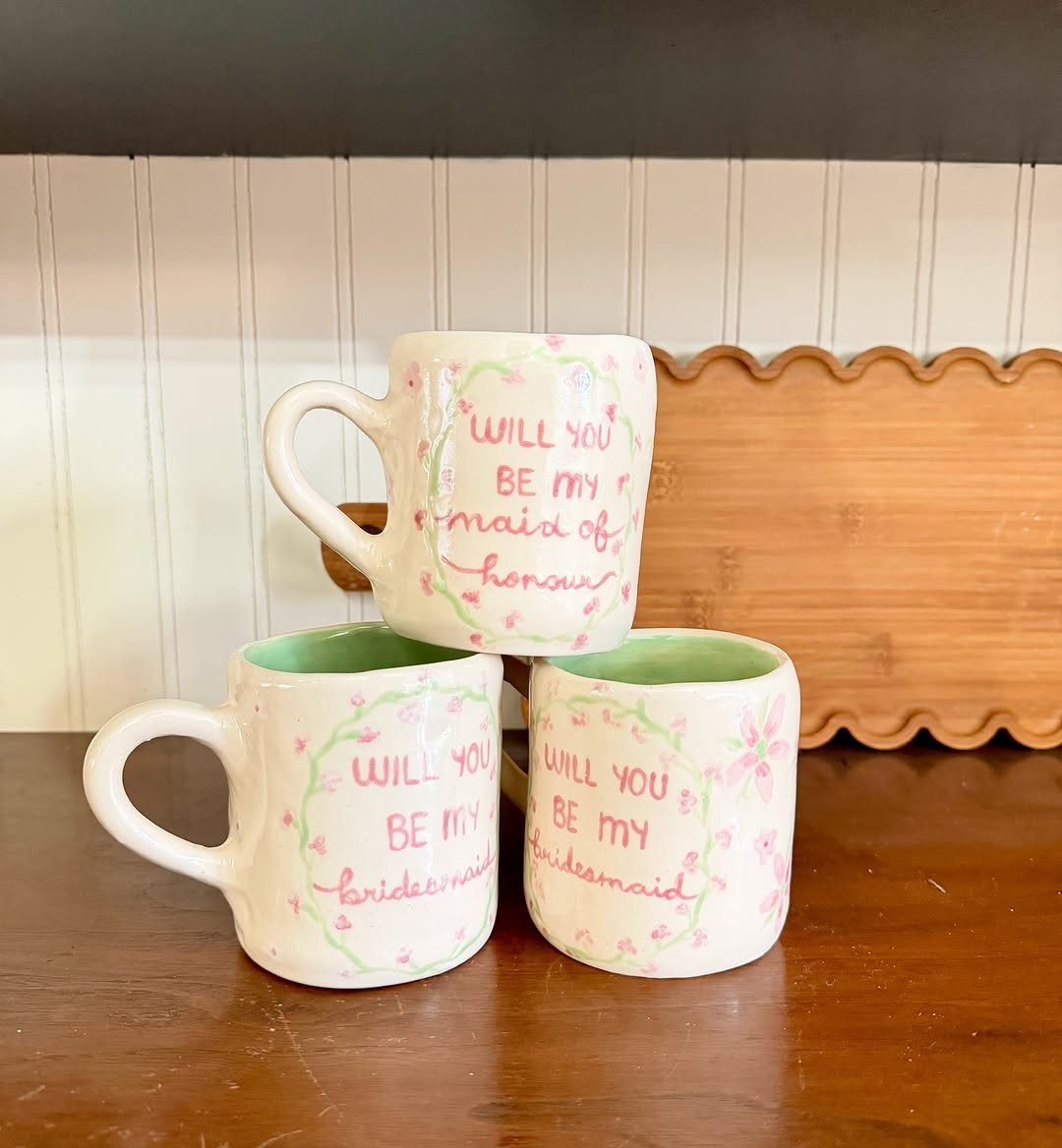 Three white ceramic mugs with pink floral designs and bridesmaid proposal text.