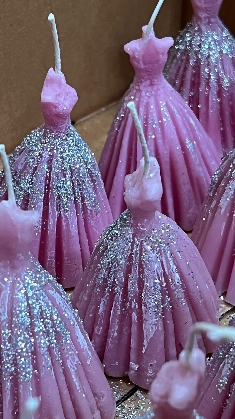 Pink dress shaped candles with silver glitter skirts arranged in a group.